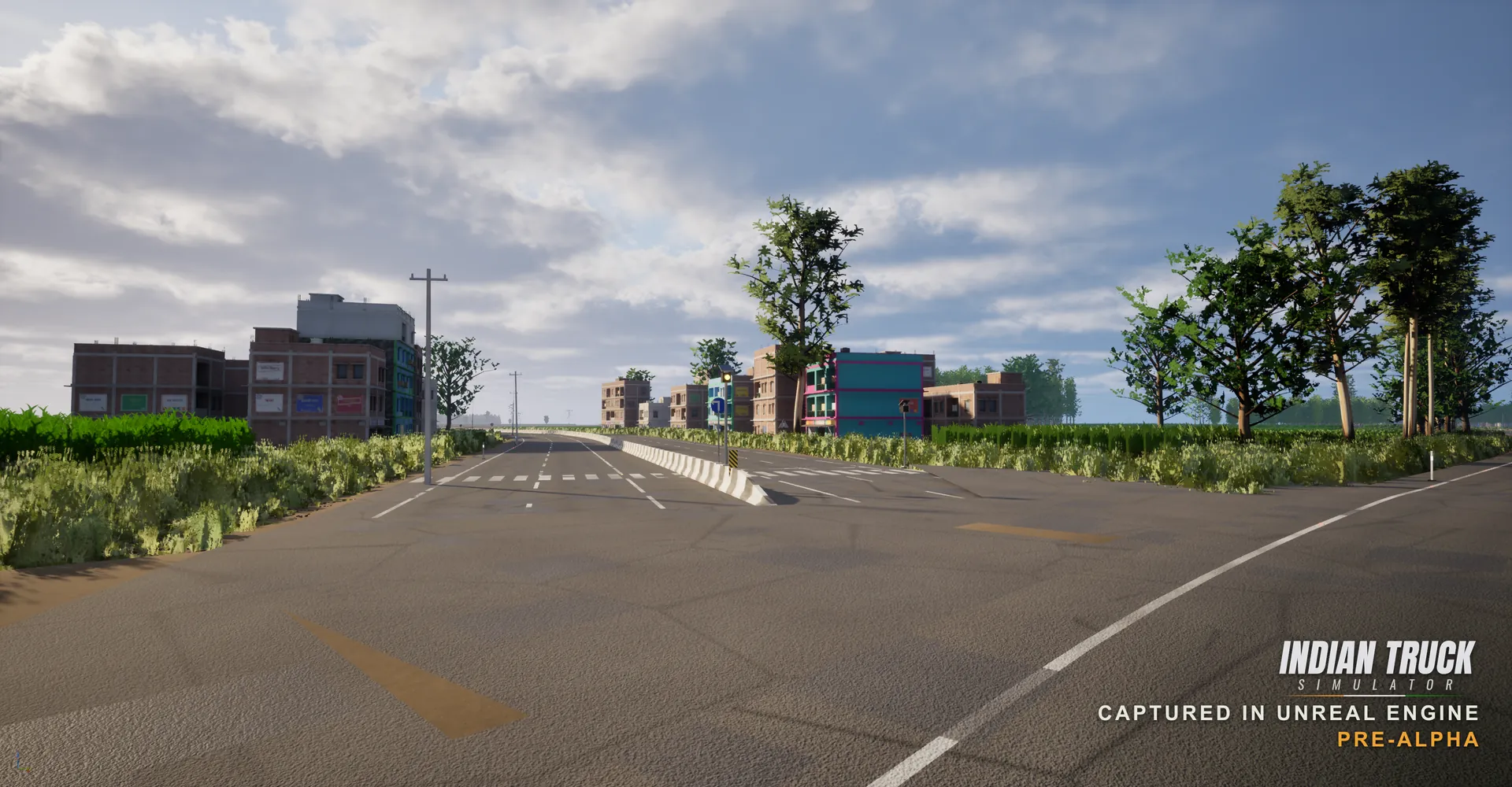 In-engine screenshot of a divided road entering a small Indian town, with multi-storey brick buildings, a brightly painted teal and pink building, hoardings and roadside greenery