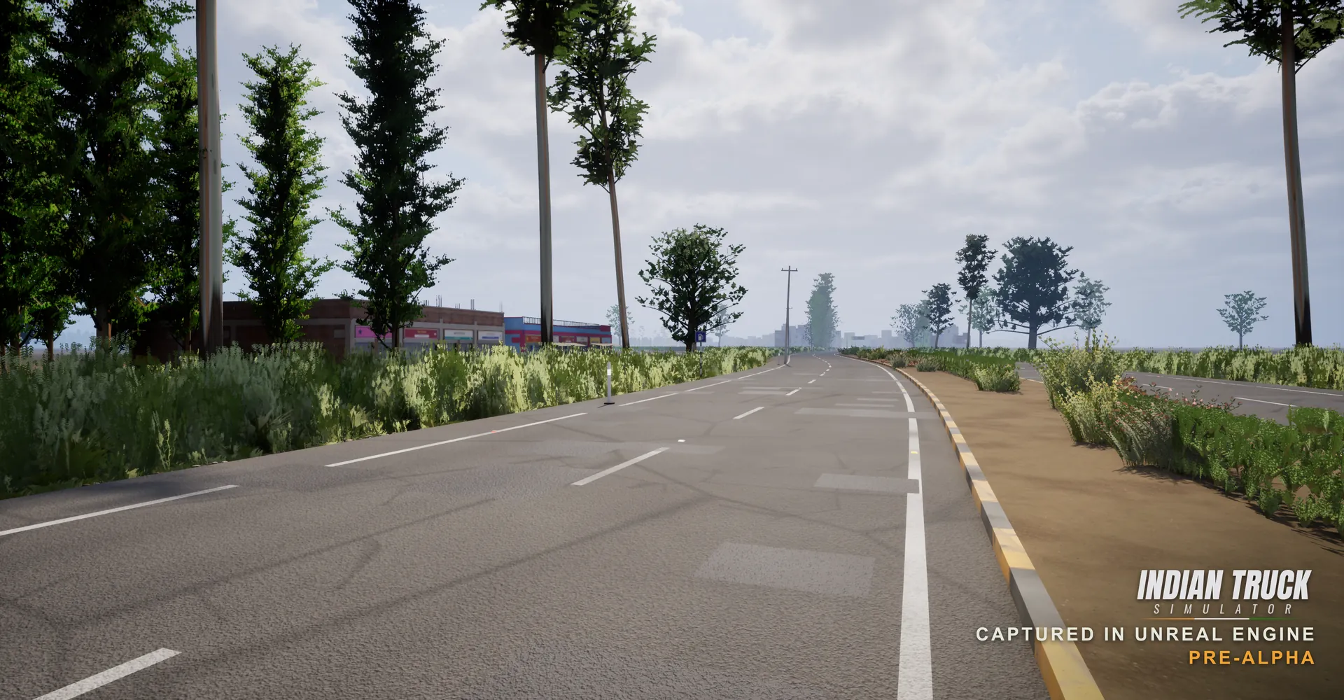 In-engine screenshot of a tree-lined Indian highway with yellow and black kerbstones, a dirt median, roadside shops and a hazy town skyline in the distance